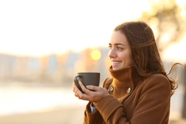 istock Happy woman drinks coffee in winter looking away on the beach 1299850830