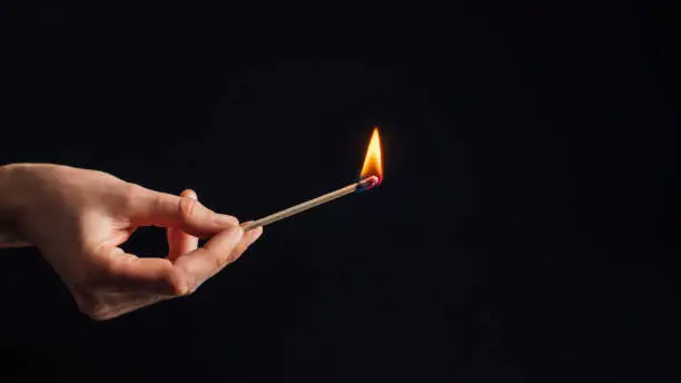 Hand holding a burning match, isolated on black background