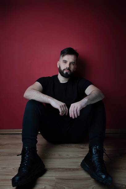 istock Dark haired man in black with beard posing on red background 1299851951