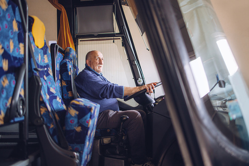 Senior man sits behind the wheel of a bus and drives a bus.