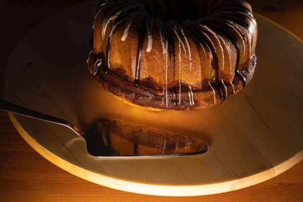 brown sugar coated brundt cake on a white turntable with silver cake shovel, image is focused on the front of the cake and the shovel, warm low light atmosphere - dark chocolate audio imagens e fotografias de stock