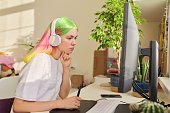 Girl teenager artist in headphones drawing on computer using graphics tablet