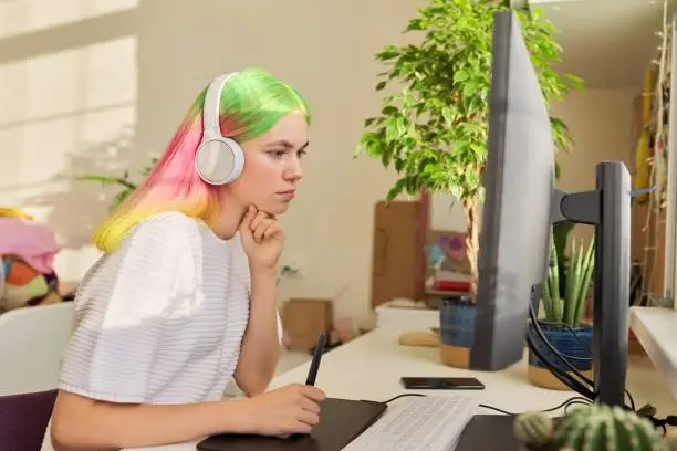 Photo of Girl teenager artist in headphones drawing on computer using graphics tablet