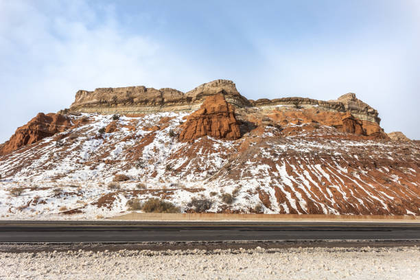 istock Looking up at red and brown mountain plateau with snow along empty highway on cloudy day in rural New Mexico 1299856818