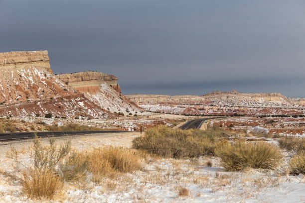 istock Long empty highway cutting through red rock valley covered in snow with mountains and overcast sky in rural New Mexico 1299856856