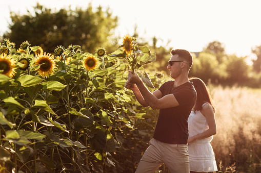 Beautiful couple having fun in sunflowers field. A man and a woman in love walk in a field with sunflowers, a man hugs a woman. selective focus.