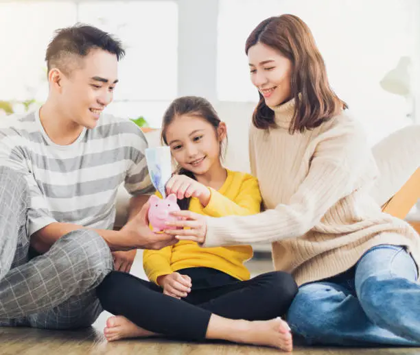 Photo of Father, mother and daughter holding a piggy bank and money  at home. Family and saving for future concept.