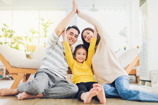 Happy family forming house roof with their hands at home