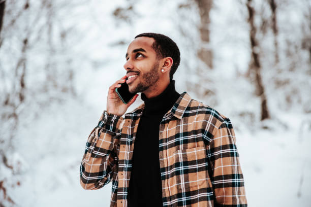 sorridente giovane nero che parla al cellulare all'interno della foresta invernale della neve - cold discussion outdoors snow foto e immagini stock