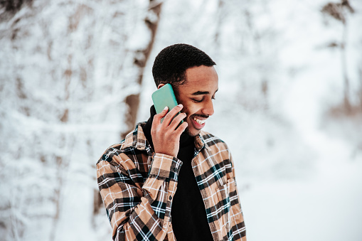 Laughing young black man having a phone call outdoors in winter on his mobile phone. Talking, laughing and having a good chat. Millennial Generation Real People Outdoor Lifestyle Portrait.
