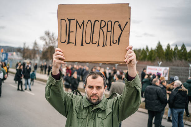 istock Angry protestor holding a banner with text Democracy on a street 1299865497