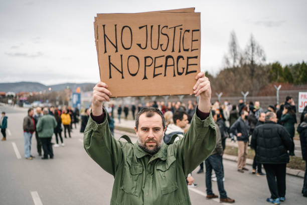 istock Angry man protesting on a street holding a banner with text No justice no peace 1299865586