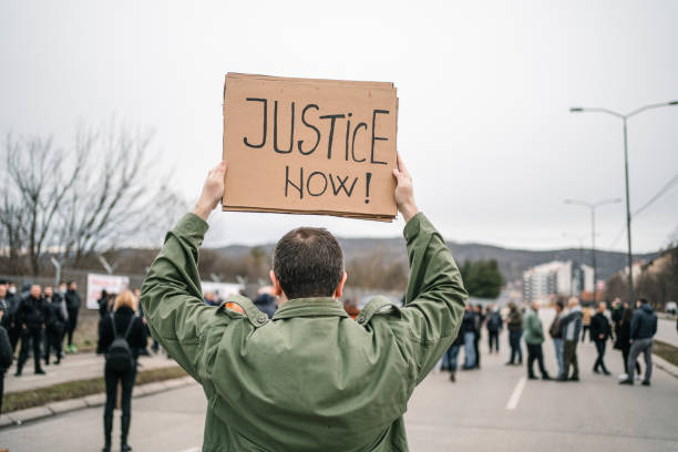 istock Unrecognizable man protesting on a street holding a banner with text Justice now 1299865605