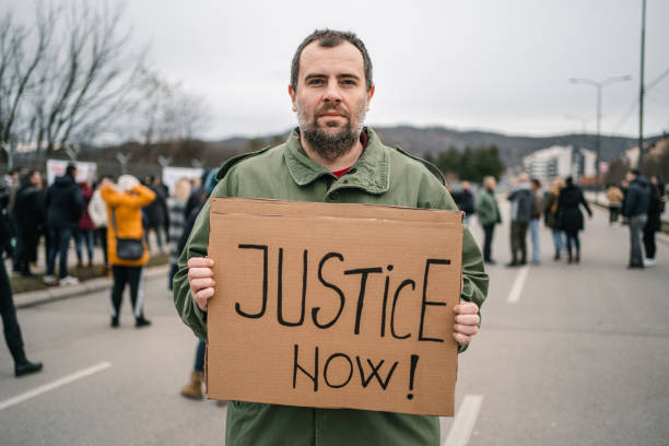 istock Man protesting on a street holding a placard with text Justice now 1299865623
