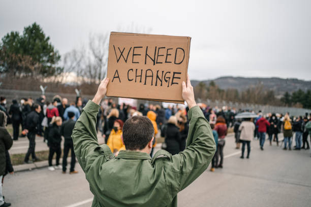 istock Unrecognizable man protesting on a street holding a banner with text We need a change 1299865719