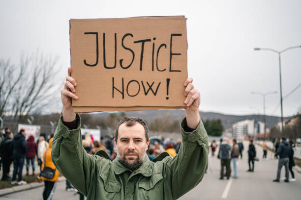 istock Man protesting on a street holding a sign with text Justice now 1299865744