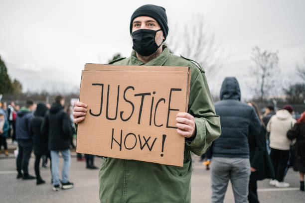 istock Man with protective mask holding a banner with text Justice now during a protest 1299865819