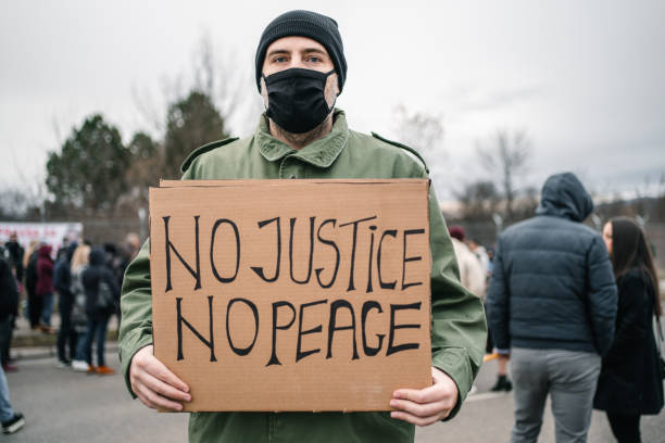 istock Young man with protective mask holding a sign with text No justice no peace 1299865844