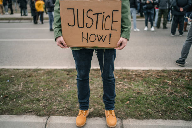 istock Unrecognizable man protesting on a street holding a banner with text Justice now 1299865885