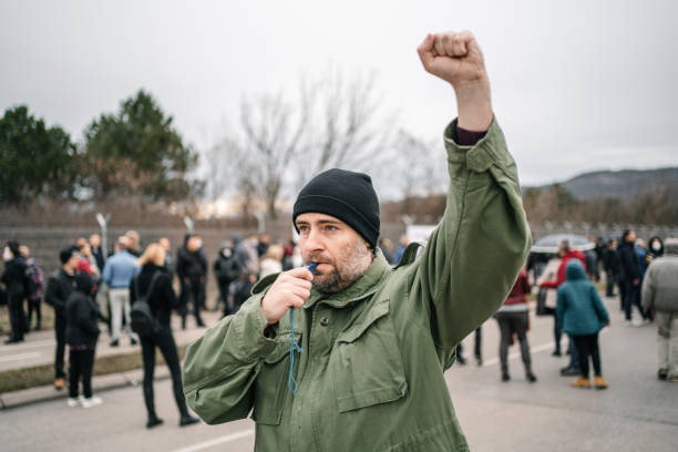 istock Man with raised fist protesting on a street blowing a whistle 1299866442