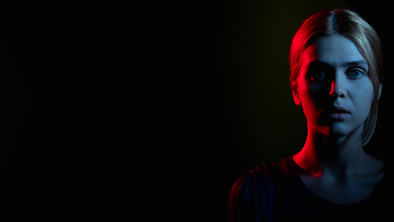 Portrait of expressionless young woman with serious posture in front of black background.