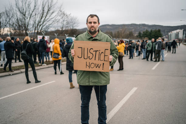 istock Man protesting on a street holding a banner with text Justice now 1299866648