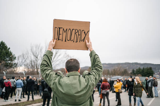 istock Man protesting on a street holding a placard with text Democracy 1299866799