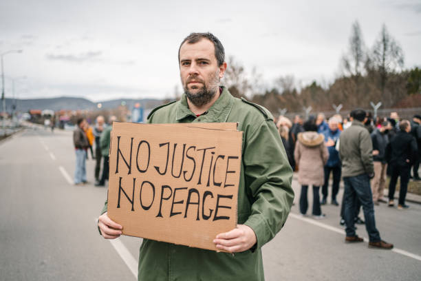 istock Man protesting on a street holding a placard with text No justice no peace 1299866920
