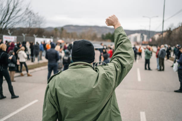 istock Man with raised fist protesting in a street 1299867010