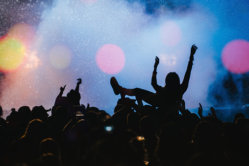 Shot of a silhouette of a young man crowd surfing as a band plays one of her favorite songs