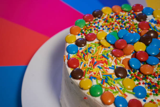 istock front shoot Cake of sponge cake and cream covered with multicolored candies served on a white plate. rainbow background. birthday or holidays 1299871656