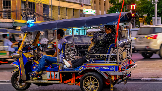 A local driver waits for passengers in his tuk-tuk on a city street in downtown Hanoi, Vietnam