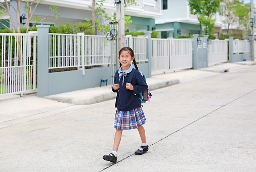 Cheerful asian little child girl in kindergarten uniform walking on street leave home to go to school at morning