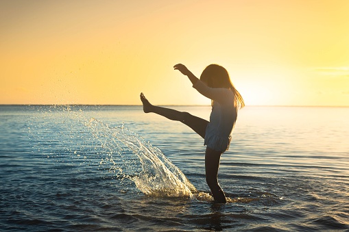 A little girl splashing and playing with water. Energetic people having fun in the summer ocean beach during sunset.
