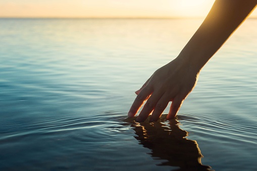 Gente feliz en la naturaleza. Una mujer sintiendo y tocando el agua del océano durante la puesta del sol. photo