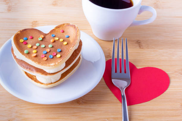 istock Homemade heart shaped pancakes with sugar decoration on a white plate, a fork, a mug with coffee or cocoa 1299889768