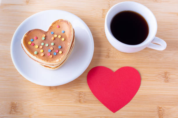 istock Homemade heart shaped pancakes with sugar decoration on white plate, fork, mug with coffee or cocoa and heart 1299889780