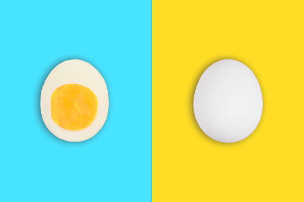 istock Raw chicken egg in shell on yellow background and boiled cut easter egg on blue background 1299889957