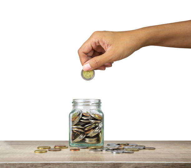 A hand holding European money coin saving to bottle jar with the coins on wooden table, white background, isolated and clipping path stock photo
