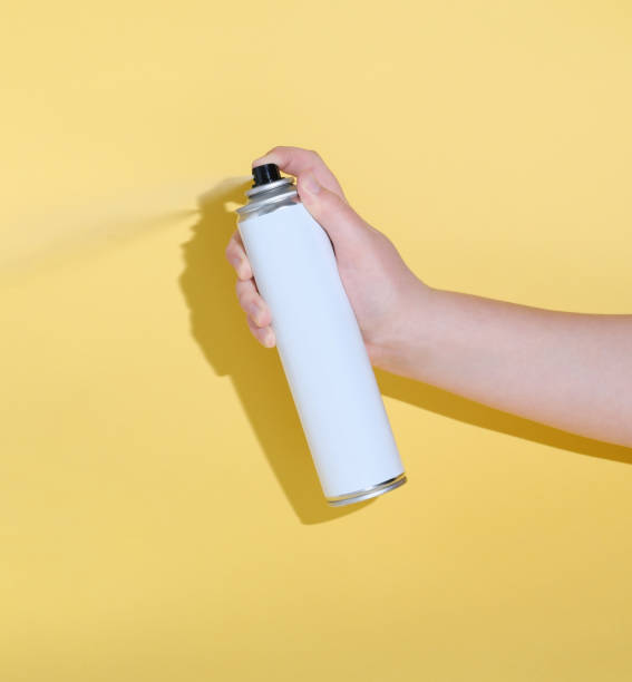 istock hand holding a tin can and spraying a product over yellow background. 1299894735