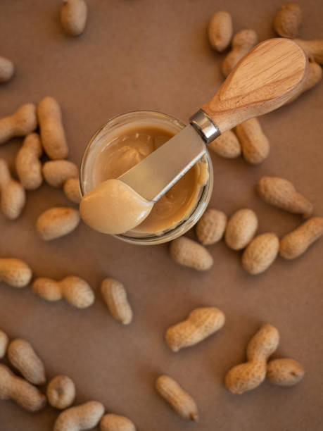 istock Homemade peanut butter in a glass jar with peanuts in shells scattered around on a craft background 1299897636