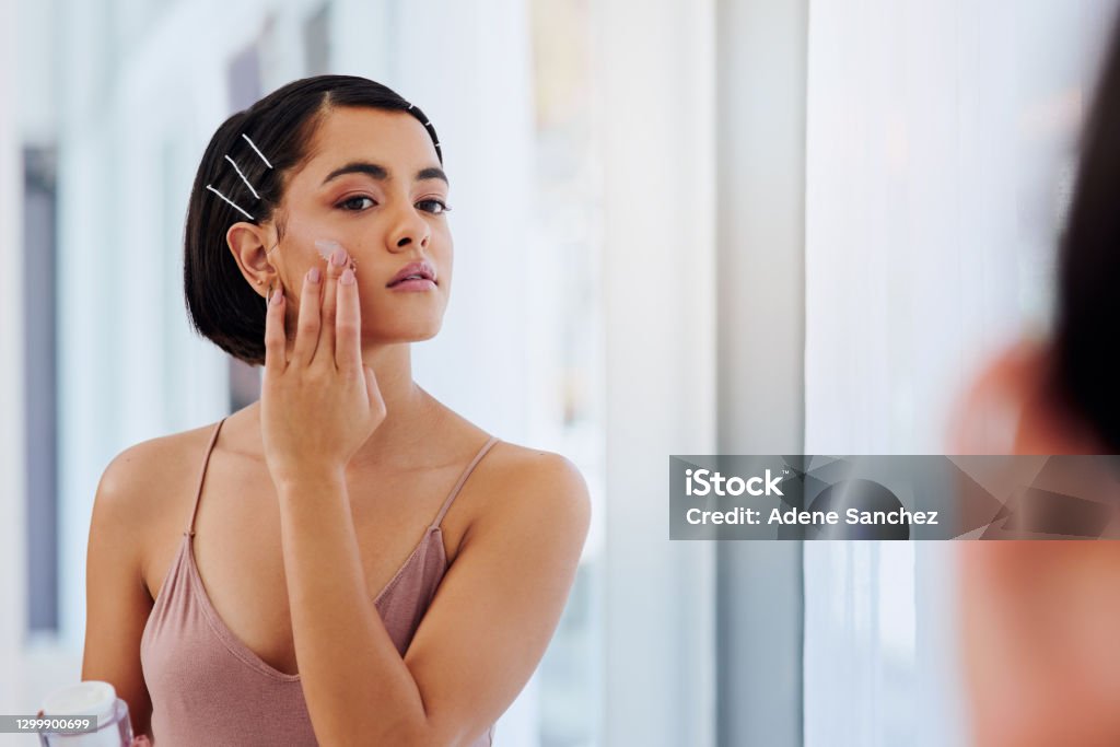 As gentle on my skin as it should be Shot of an attractive young woman applying moisturiser in front of a bathroom mirror Skin Care Stock Photo