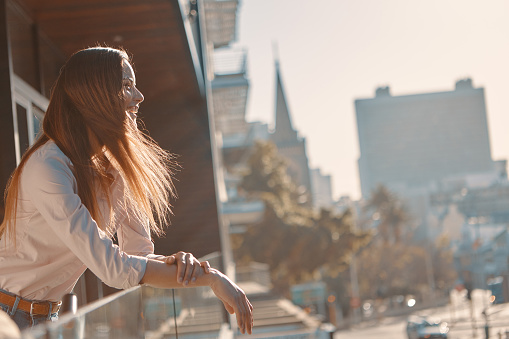 Shot of a beautiful young woman standing on a balcony against an urban background