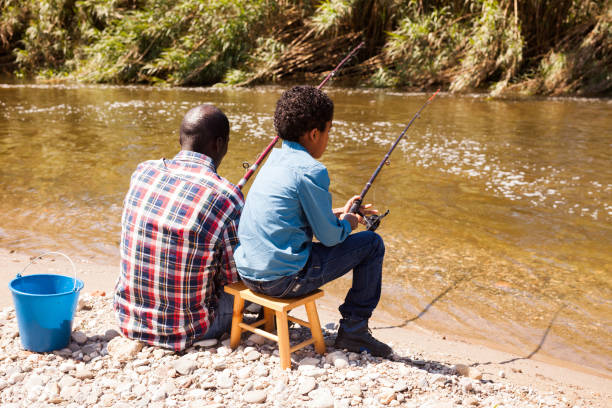 istock Man and little boy sitting near river 1299902018