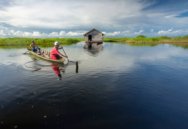 dos chicos están remando su barco en un estanque tranquilo con cielo azul brillante en el fondo - jukung fotografías e imágenes de stock