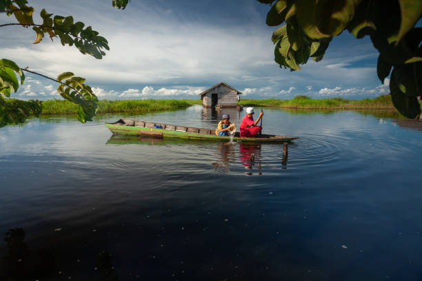 dos chicos están remando su barco en un estanque tranquilo con cielo azul brillante en el fondo - jukung fotografías e imágenes de stock