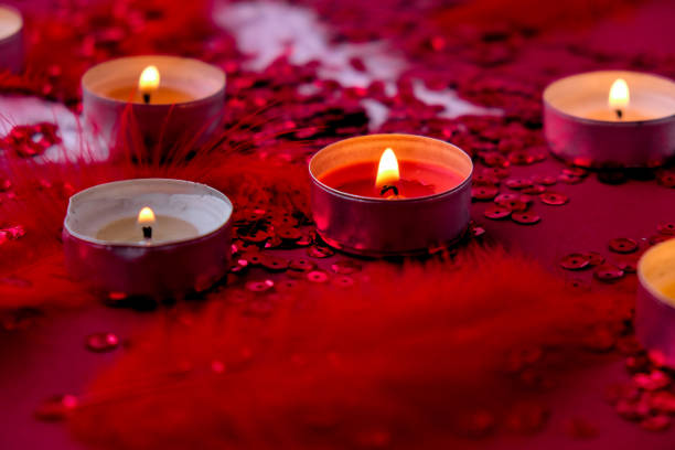 Burning red candles on Red shiny confetti sequinned background with feathers. Saint Valentines Day and Christmas background . Holidays background and textures.