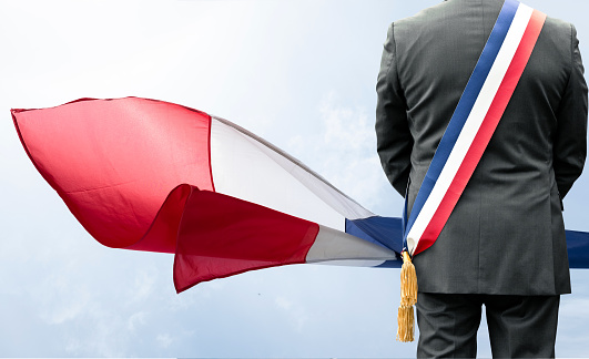The French tricolor flag that flies in the wind with a mayor and his scarf