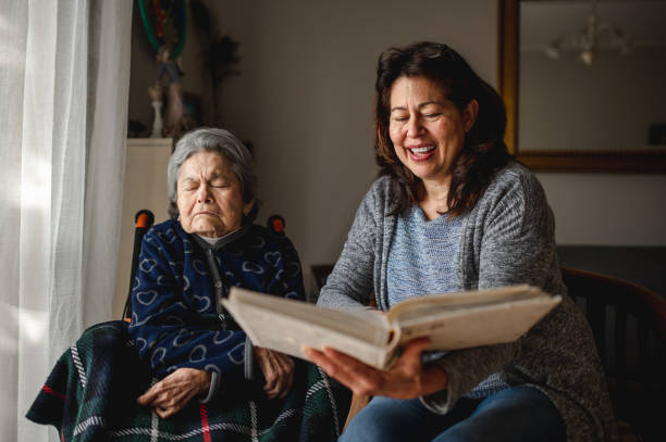 Old sick woman with memory loss sitting in wheelchair. Old sick woman with memory loss sitting in wheelchair. Smiling daughter holding a photo album trying to remember. nursing home photos stock pictures, royalty-free photos & images