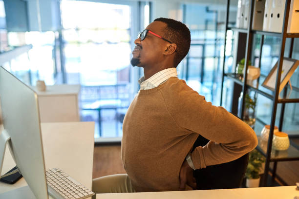 How do I put a stop to this pain? Shot of a young businessman experiencing back pain while working in an office office back pain stock pictures, royalty-free photos & images